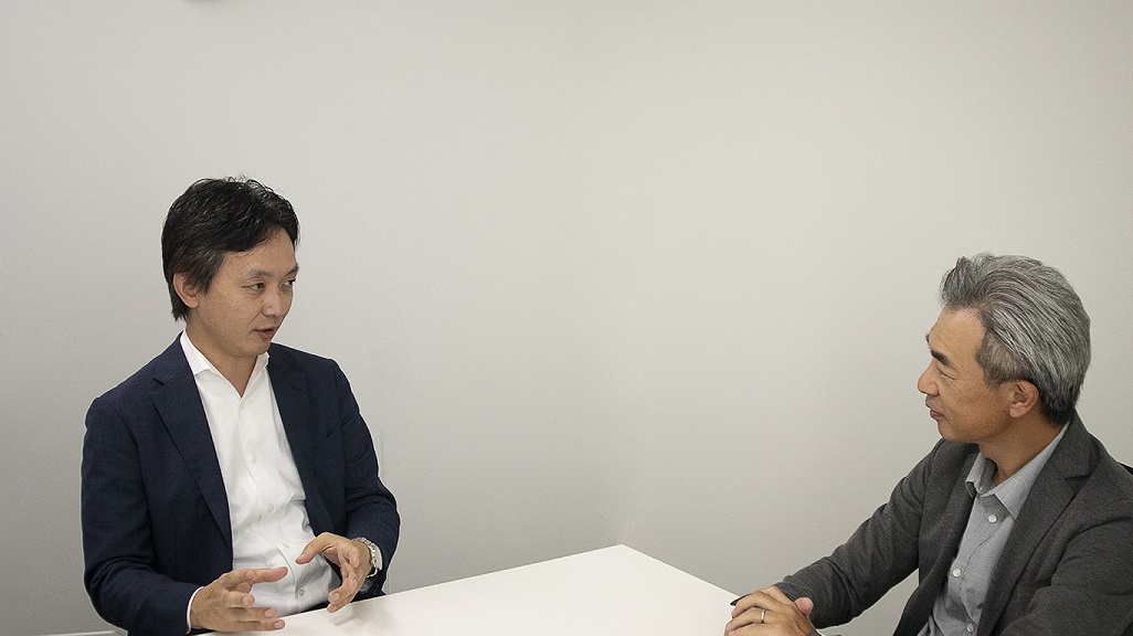男性2人が机に座って話す様子